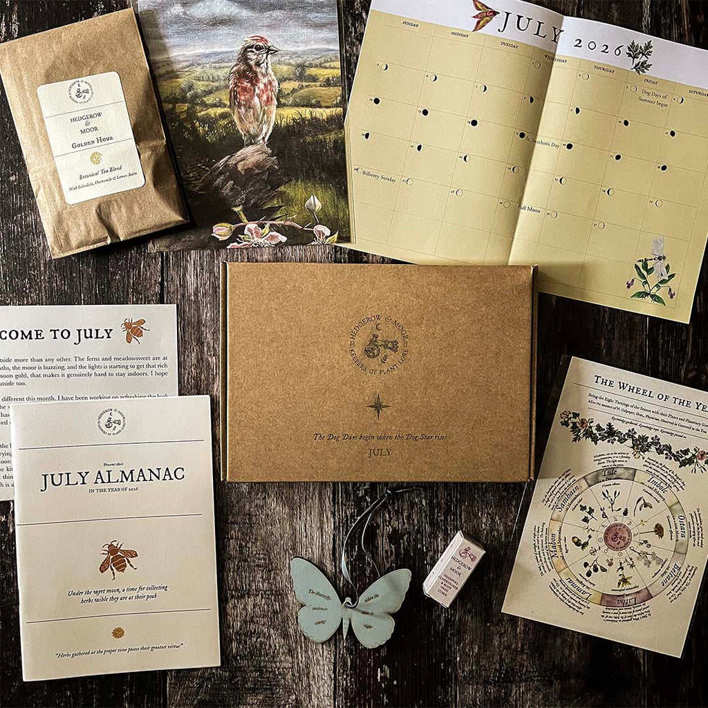 Collection of hedgerow and Moor July-themed items including a calendar, almanac, and decorative elements on a wooden surface.