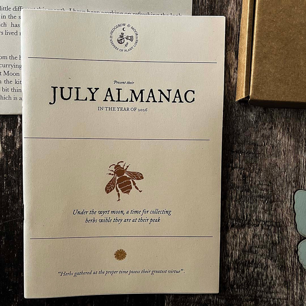 Hedgerow and Moor July Almanac on a wooden surface with a bee illustration