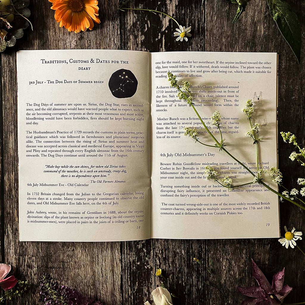 Open hedgerow and moor almanac showing customs and traditions and illustrations on a wooden surface with flowers