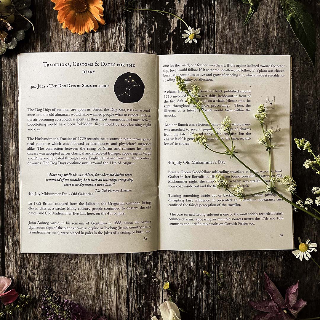 Open hedgerow and moor almanac showing customs and traditions and illustrations on a wooden surface with flowers