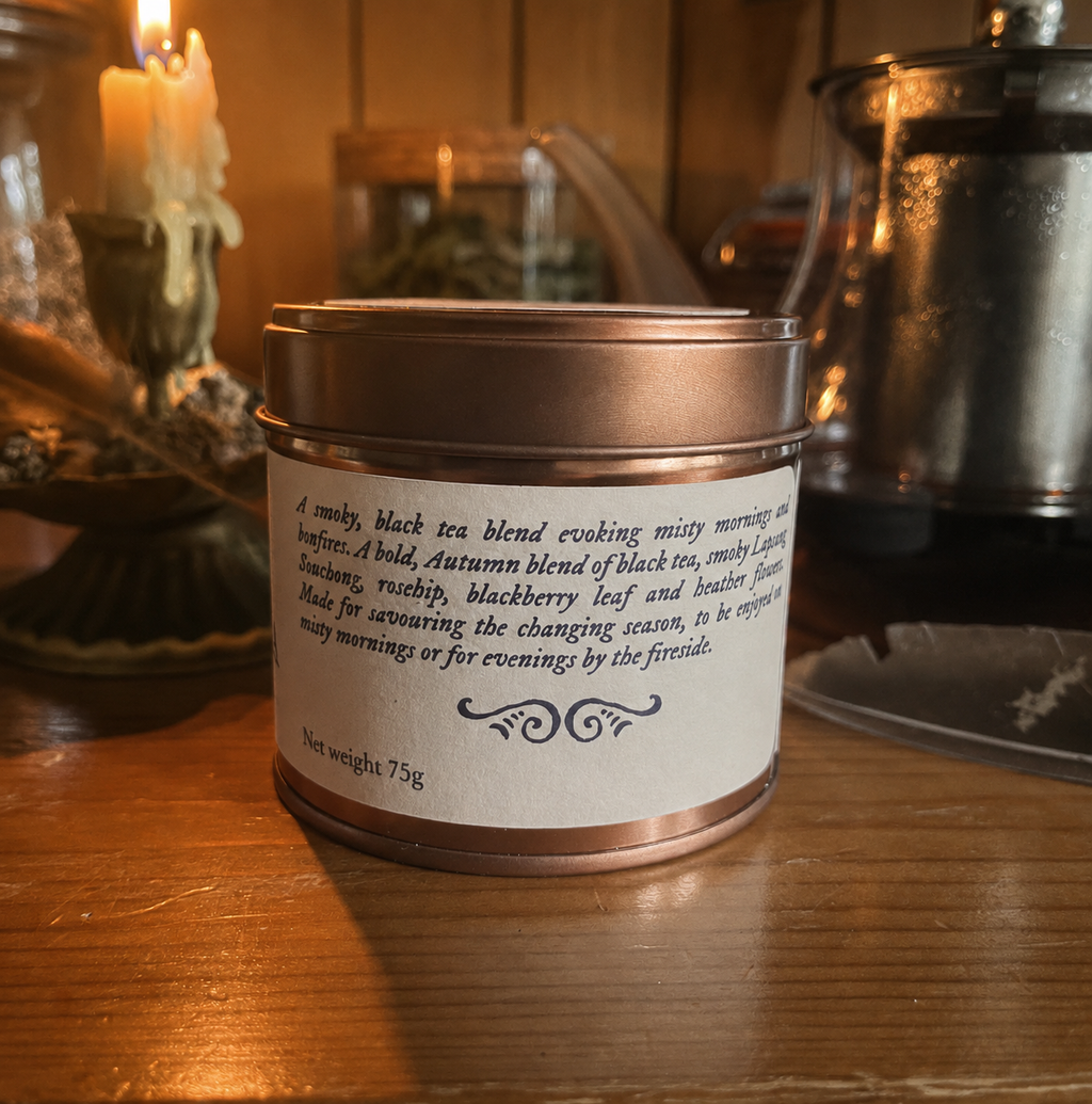 A 75g tin of smoky black tea blend with a white paper label and metallic lid, set on a wooden table with a warm, candlelit background.