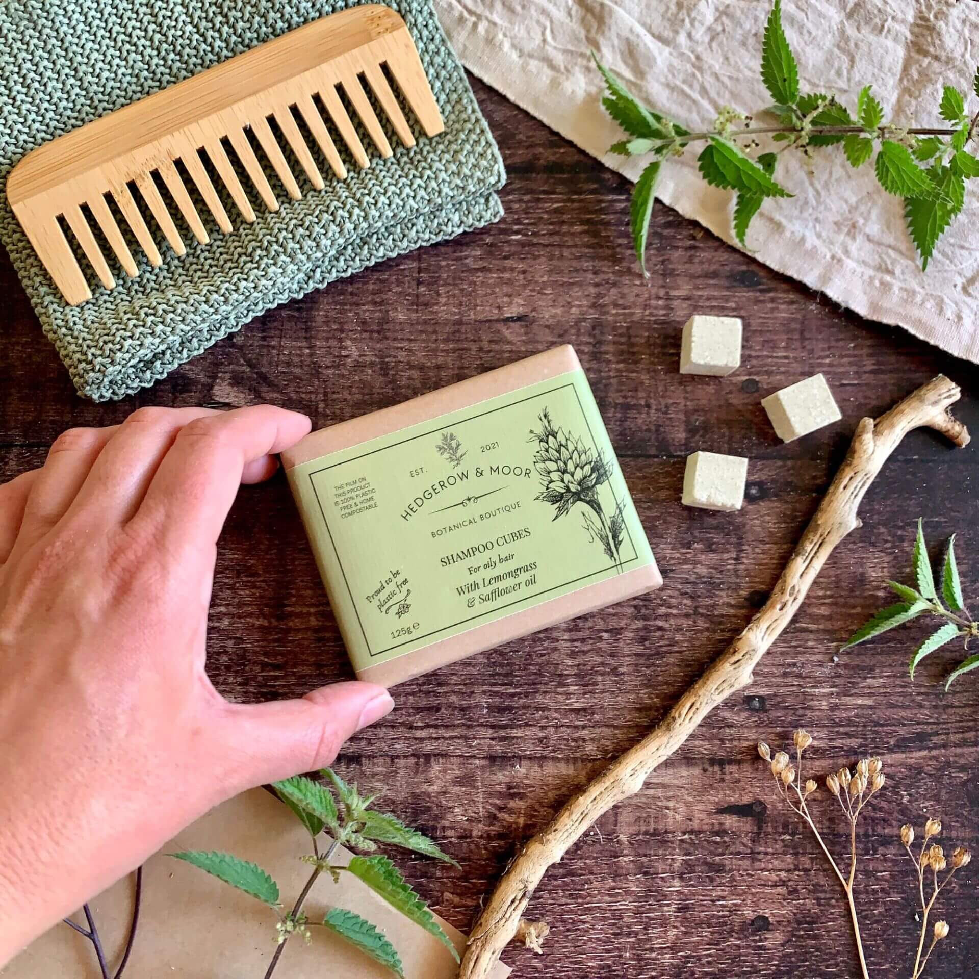 Hand holding a pack of oily shampoo cubes with natural elements on a wooden surface